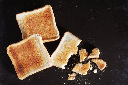 Whole and broken toasted bread on old black metal tray close-up, top view