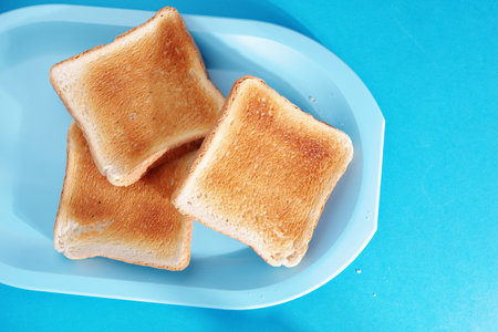 Grilled toasted bread on plastic tray on blue background, top view