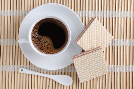 Square wafers with filling and cup of coffee on bamboo napkin, top viewの写真素材