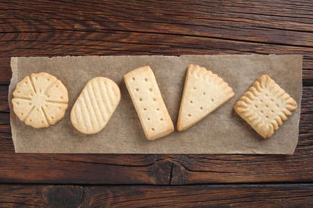 Various shortbread biscuits on brown baking paper on wooden table, top view