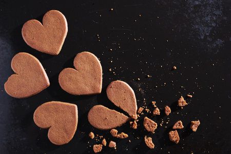Whole and broken heart shaped ginger cookies on old black metal tray, top viewの写真素材
