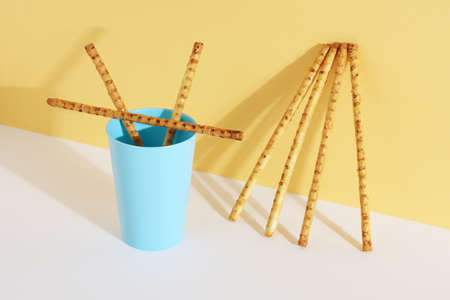 Bread sticks with sesame seeds in a blue plastic glass and near on white-yellow background
