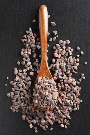 Himalayan rock salt in wooden spoon on black stone background, top viewの写真素材