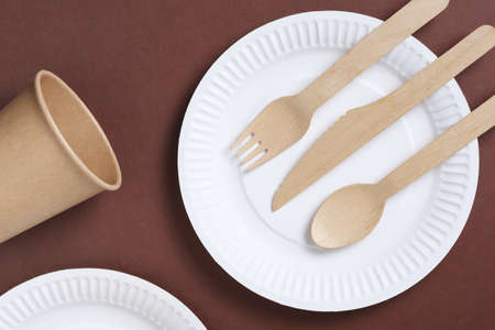 Disposable tableware and cutlery made of wood and paper on a brown cardboard background, top viewの写真素材