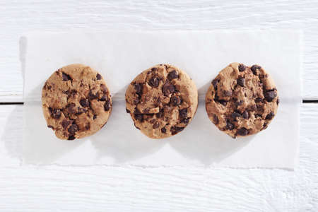 Chocolate chip cookies on a plate on wooden background with torn paper, top view