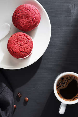 Red velvet sandwich cookies and cup of coffee on black wooden table, top viewの写真素材