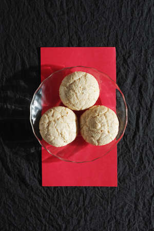 Amaretti almond cookies on a transparent plate on black fabric background, top view