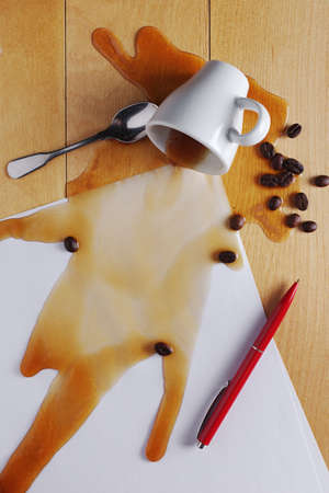 Cup of coffee spilled on sheets of white paper and a pen on the desk, top viewの写真素材
