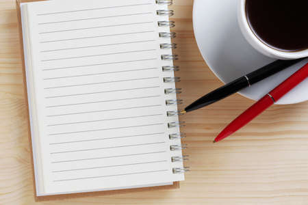Spiral notepad, cup of coffee and two pens on wooden table close up, top viewの写真素材