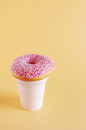 Pink donut and disposable cup of coffee on yellow background. Copy spaceの写真素材