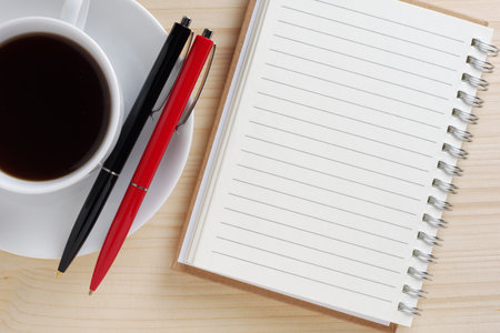 Cup of black coffee, notepad and two pens on wooden table close up, top viewの写真素材