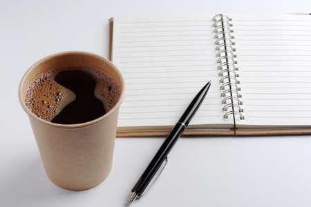 Disposable paper cup of coffee, blank notepad and pen on white backgroundの写真素材