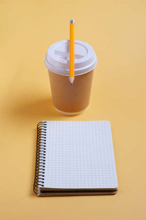 Notebook, pencil and disposable paper beverage cup on yellow background or tableの写真素材