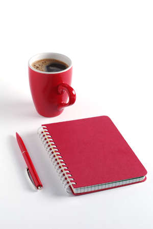 Notepad and pen with a red cup of black coffee on white backgroundの写真素材