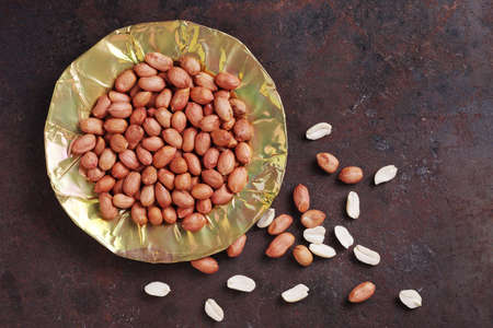Peeled peanuts on an old brass or copper plate on grunge metal background, top view