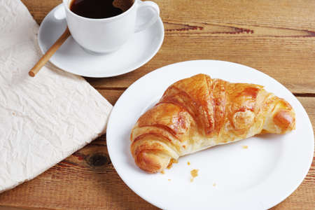 Croissant on a plate with cup of coffee on wooden table