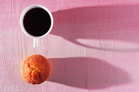 Cupcake with a cup of hot black coffee on a pink painted wooden background, top view with copy spaceの写真素材