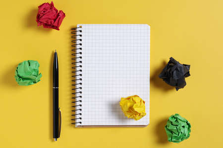 Notepad, pen and balls of colored crumpled paper on yellow background, top view