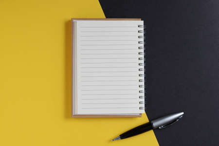 Notepad and pen on black-yellow background, top view