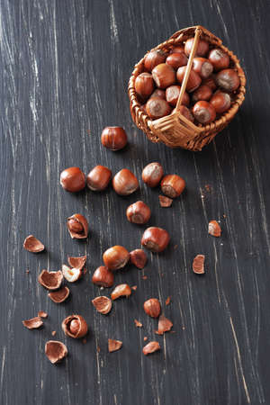 Hazelnuts in a small basket and near on a black wooden background