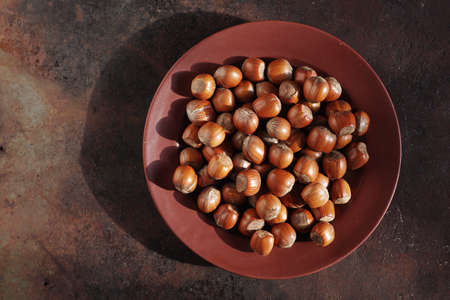 Plate with hazelnuts on rusty metal background, top view