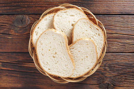 Freshly baked wheat bread slices on a wicker plate on the table, top view
