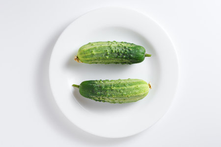 Two fresh green cucumbers on a plate on white background, top viewの写真素材