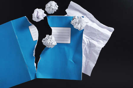 Torn school notebook and crumpled paper balls on black background, top view