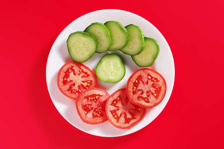 Cucumbers and tomatoes slices on a plate on red background, top viewの写真素材
