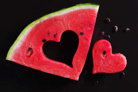 Slice of watermelon with a cut in the shape of a heart on black background, top viewの写真素材