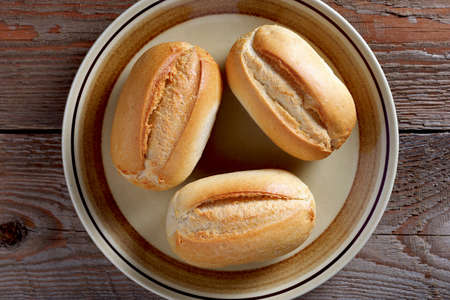 Three loaves of small wheat bread on a plate on wooden background, top view