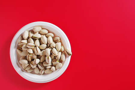 Pistachio nuts in an eco-friendly paper plate on red background, top view with copy space