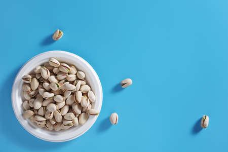 Pistachio nuts in an eco-friendly plate on blue background, top view with copy spaceの写真素材