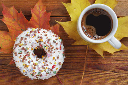 Cup of coffee and donut on wooden background with autumn leaves, top viewの写真素材