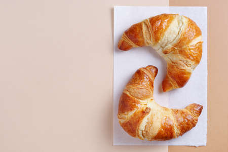 Two fresh croissants on paper background, top view with copy space