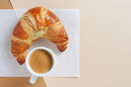 Freshly baked croissant and cup of coffee on paper background, top view with copy spaceの写真素材