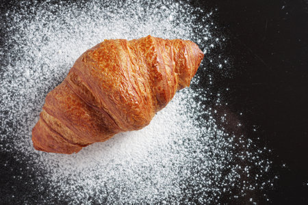 Freshly baked croissant on black background with flour, top view. Selective focusの写真素材