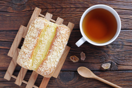Sweet bun with cream and cup of tea on wooden background, top view