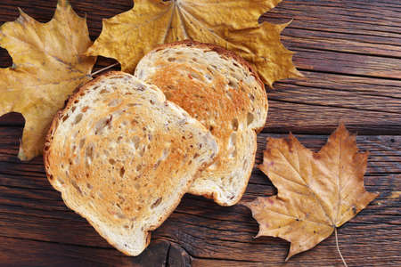 Grilled toasted bread on wooden background with autumn leaves, top view