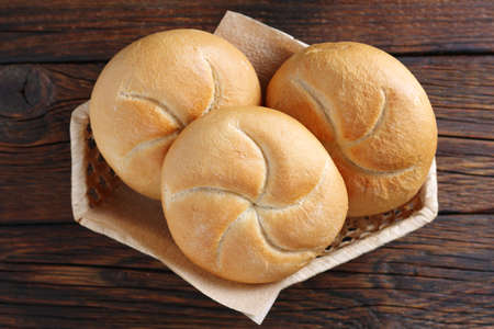 Loaves of small wheat bread on wicker bowl on wooden background, top viewの写真素材