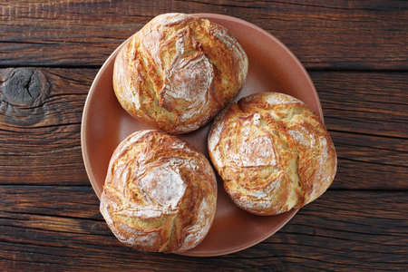 Small loaves of bread on a plate on wooden background, top viewの写真素材