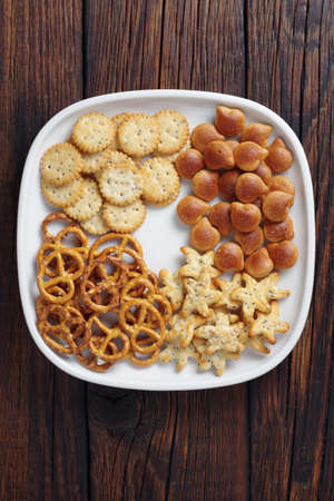 Various small crackers in plate on wooden background, top viewの写真素材