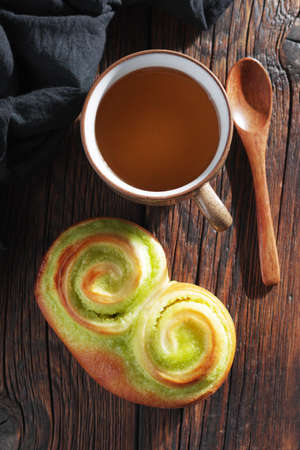 Kiwi jam bun and cup of tea on wooden background, top view