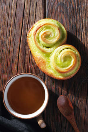 Buns with kiwi jam and cup of tea on wooden background, top view
