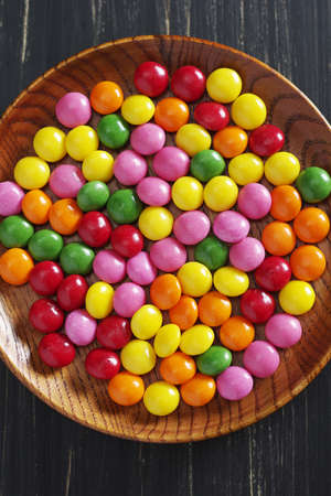 Colorful skittles candies in wooden plate on black background, top viewの写真素材