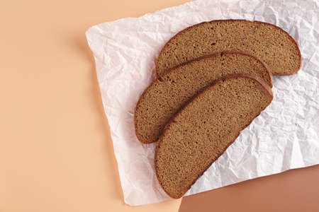 Slices of rye bread on crumpled paper on two-tone background, top view with copy space