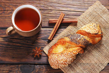Cup of tea and puff pastry bun with seeds on wooden background, top view