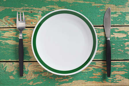 Empty clean plate with cutlery on old green wooden table, top view