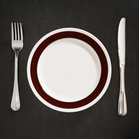 Empty clean plate with cutlery on black stone background, top viewの写真素材