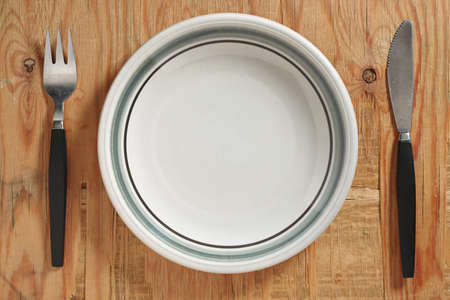Plate with knife and fork on old wooden table, top view